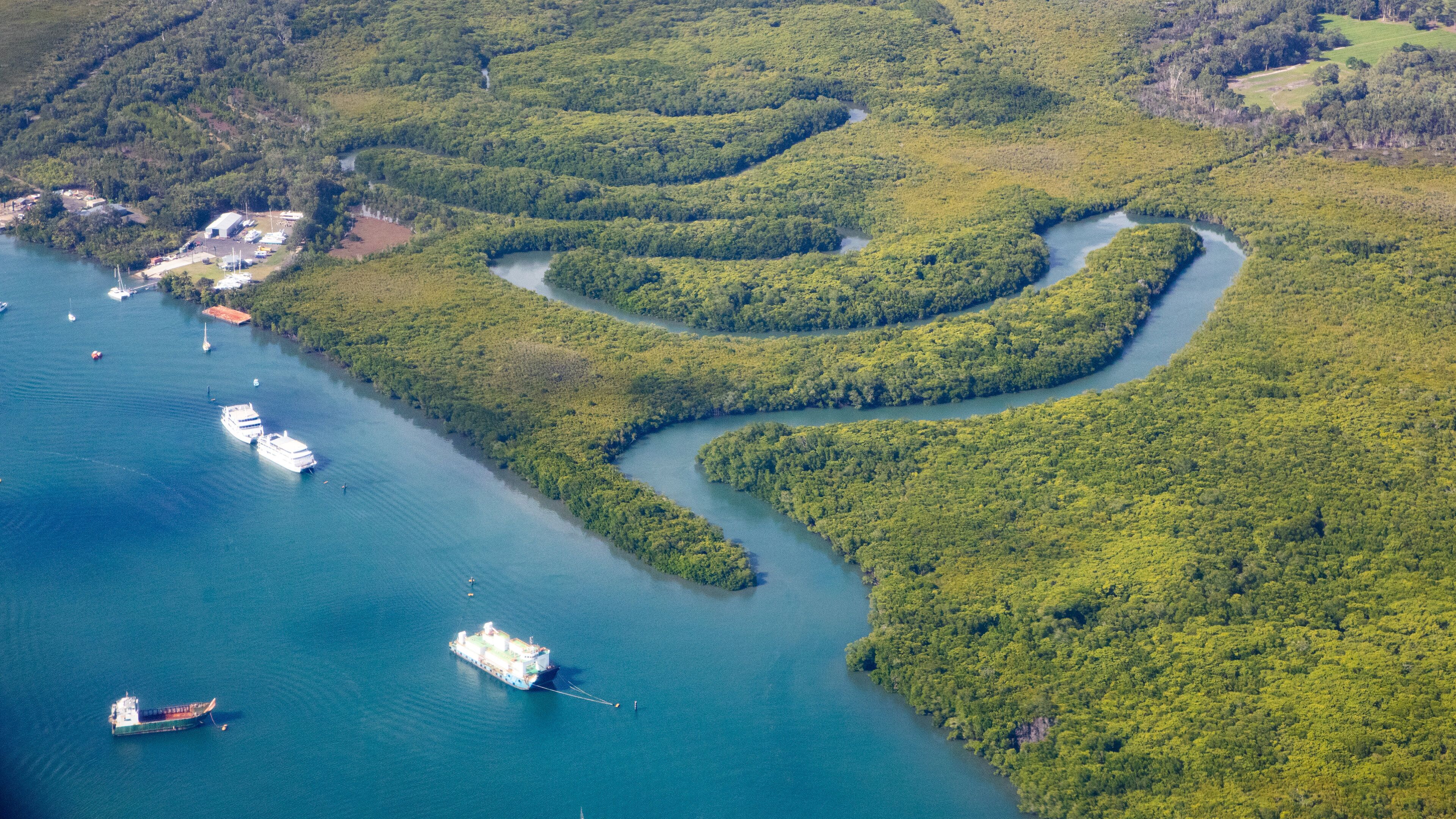 An aerial view of a river winding through a dense forest with several boats and a dock area.