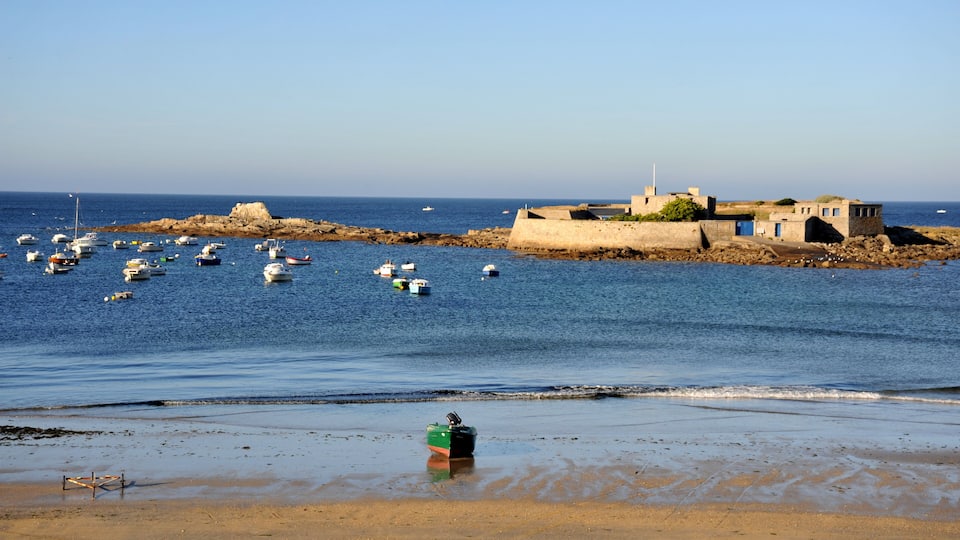 A coastal scene with boats, a sandy beach, and a fortified structure with a lighthouse.