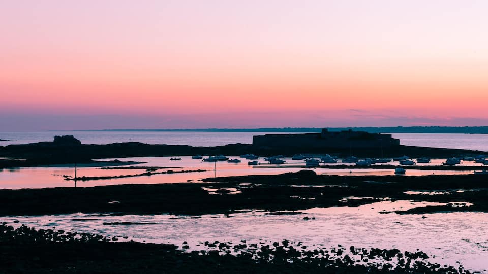 A coastal landscape at sunset with rocky formations and calm waters.