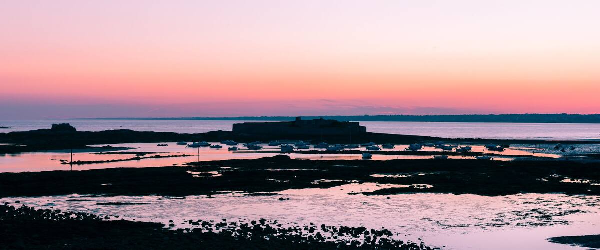 A coastal landscape at sunset with rocky formations and calm waters.