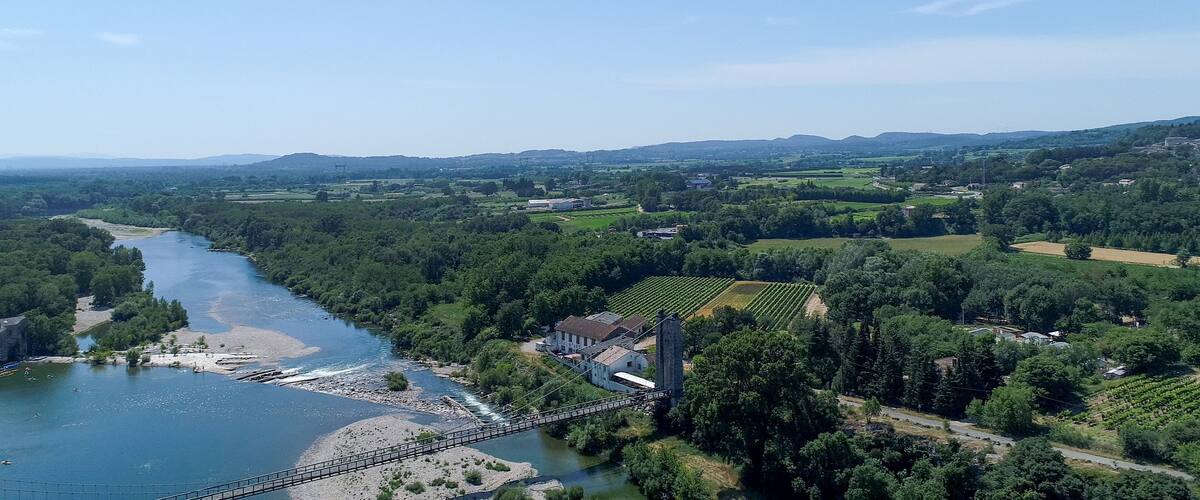 A river flowing through a valley with a bridge, surrounded by lush greenery and distant hills.