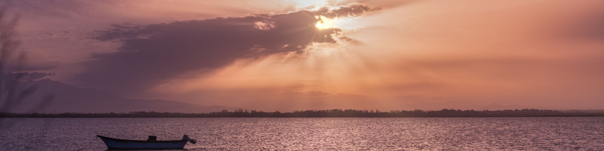 boat on the background of the sunset with rays breaking through the clouds on proud in Canet-en-Roussillon