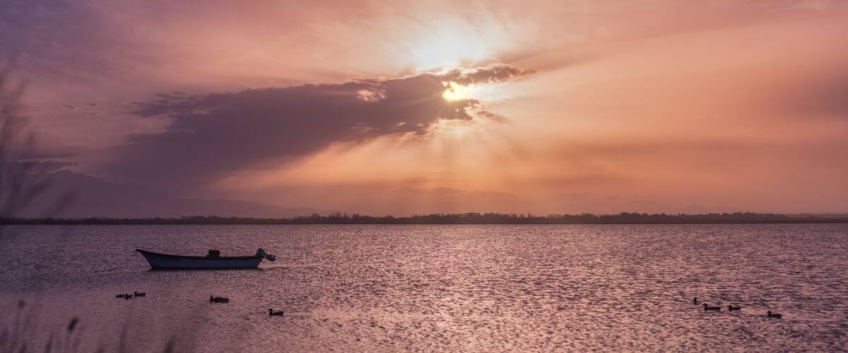 A boat on calm water with a sunset and mountains in the background.