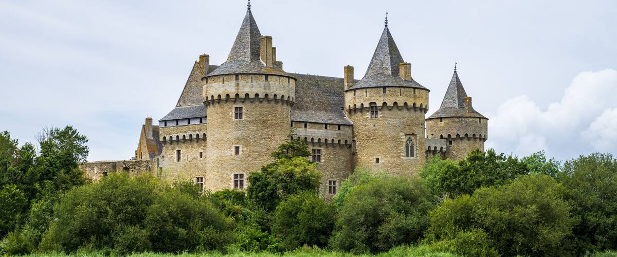 A medieval castle with multiple towers and surrounded by lush greenery.