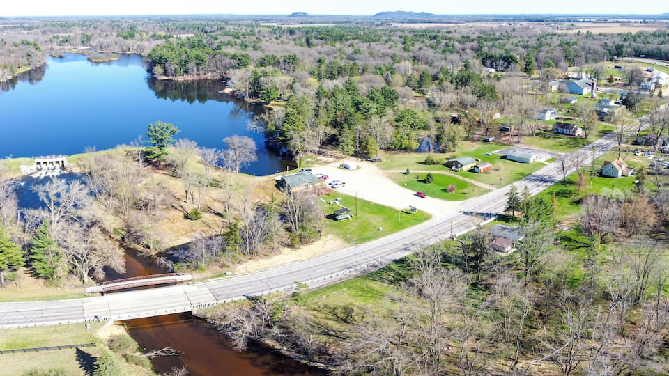 A bridge over a river, surrounded by trees and a small community with houses and a parking lot.