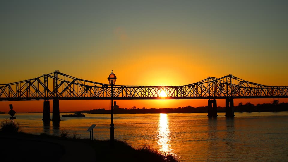 A bridge silhouetted against a sunset over a river.