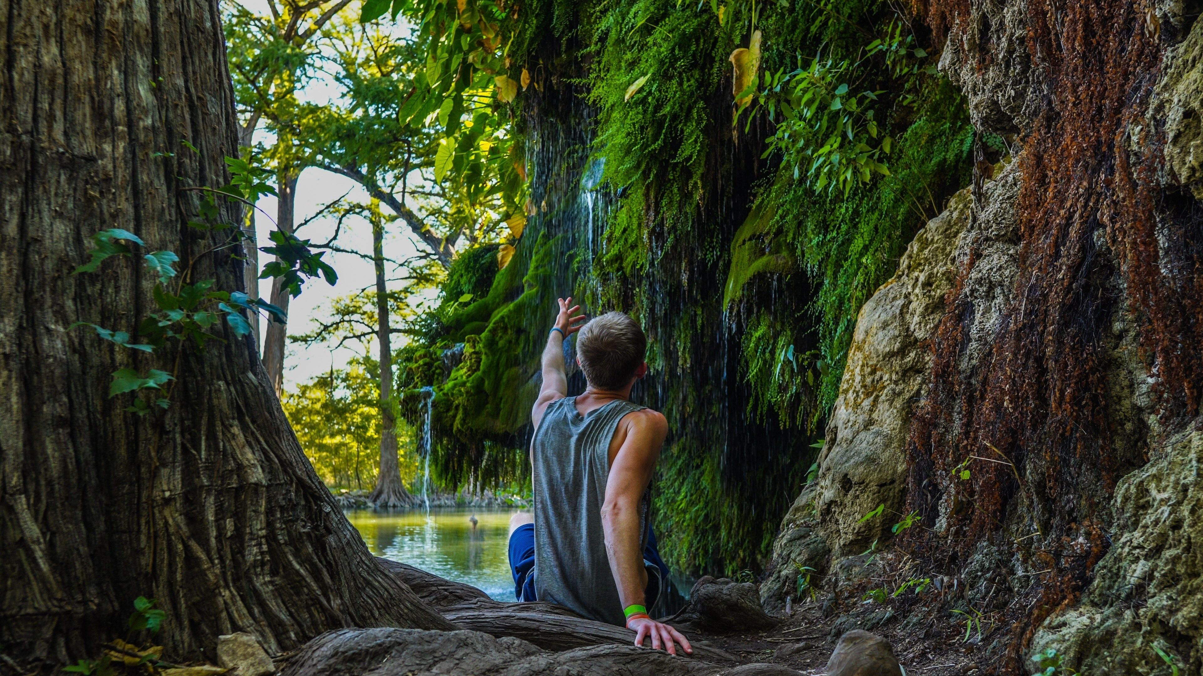 Man reaching to waterfall at Krause Springs Waterfall near Austin, TX