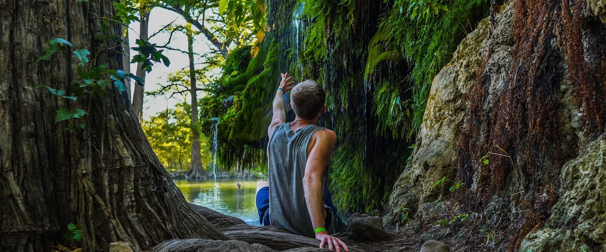 Man reaching to waterfall at Krause Springs Waterfall near Austin, TX