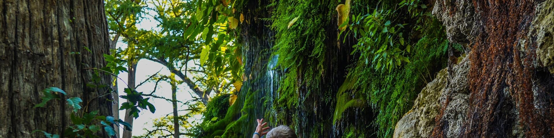 Man reaching to waterfall at Krause Springs Waterfall near Austin, TX