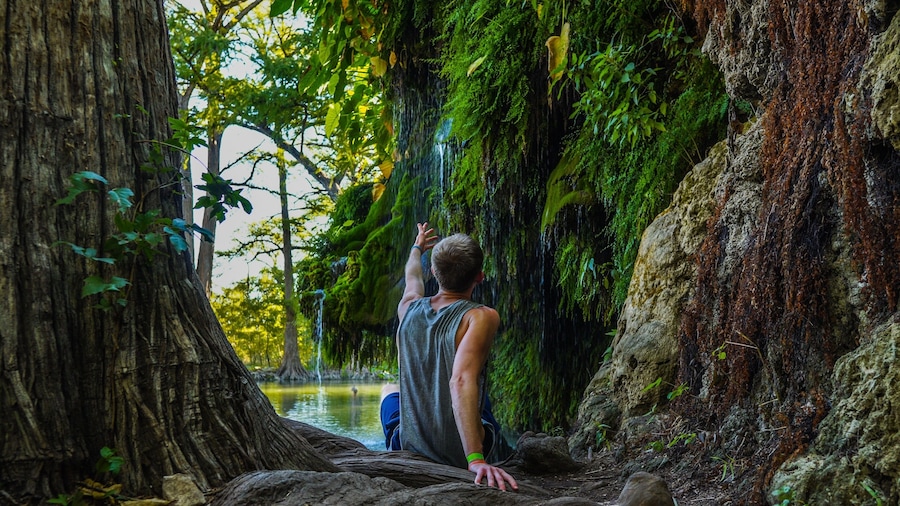 Man reaching to waterfall at Krause Springs Waterfall near Austin, TX