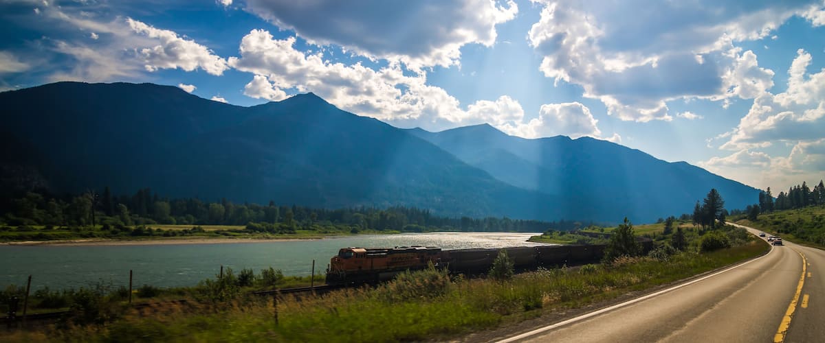 A train on a bridge over a river, surrounded by mountains and a clear sky.