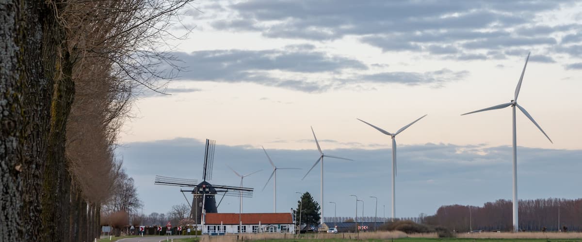 A road with wind turbines and a traditional windmill in the background.