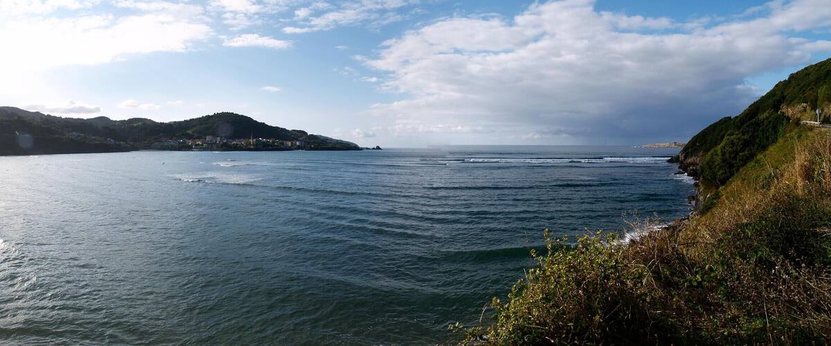 A coastal landscape with a sandy beach, calm sea, and a hill with vegetation.