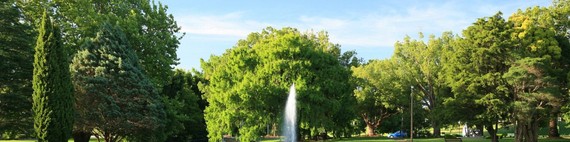 A park with a fountain, lush green grass, and trees.
