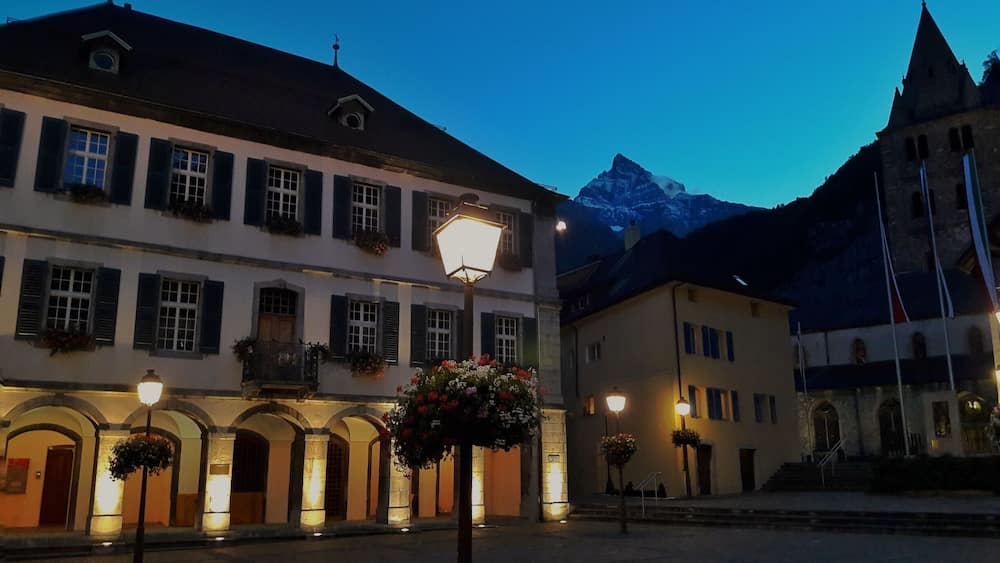 Une place historique bordée de bâtiments illuminés, avec une montagne en toile de fond.