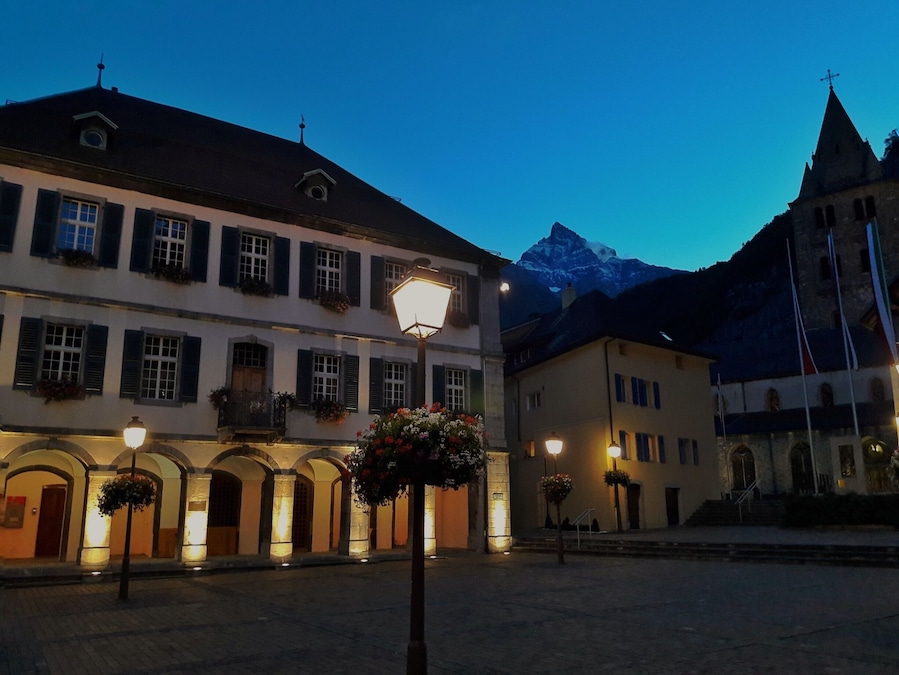 Ein historischer Stadtplatz mit beleuchteten Gebäuden und einem Berg im Hintergrund.