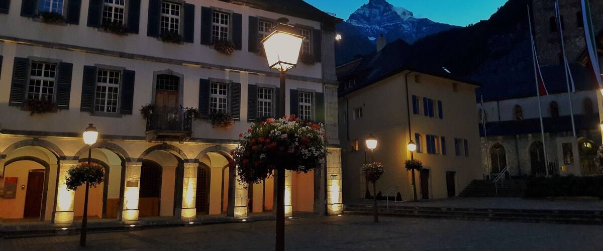 A historic town square with illuminated buildings and a mountain in the background.