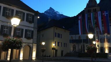 A town square with buildings, street lamps, and flags.