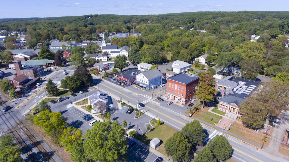 An aerial view of a town with a mix of residential and commercial buildings, a railway track, and a green park area.