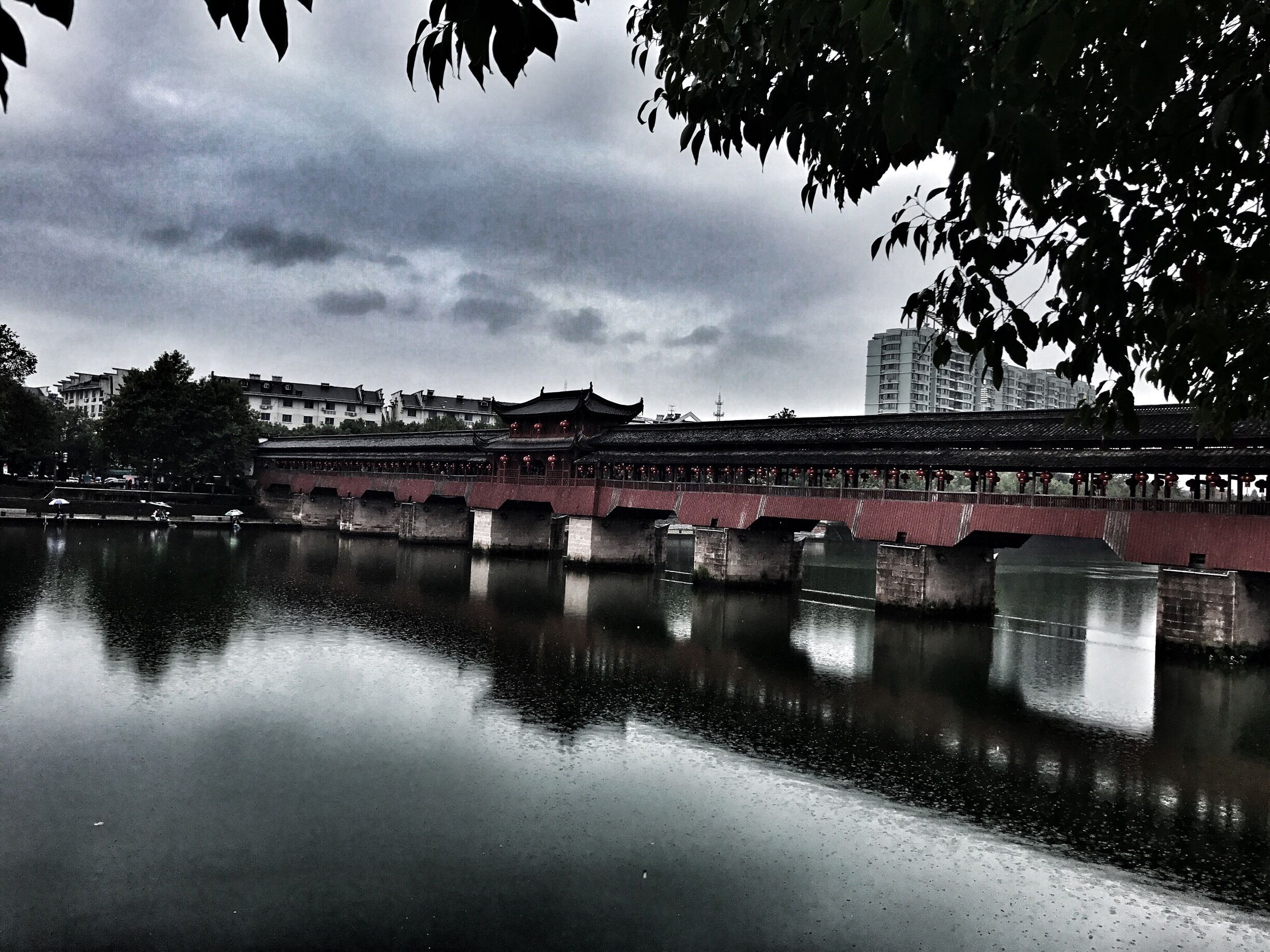 A traditional bridge over a calm river, with buildings and trees in the background.