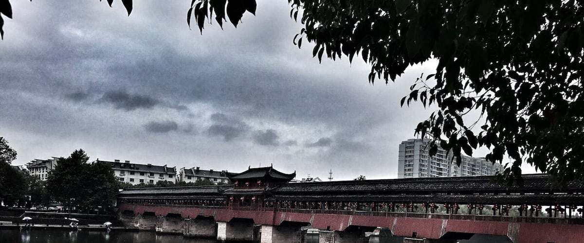 A traditional bridge over a calm river, with buildings and trees in the background.