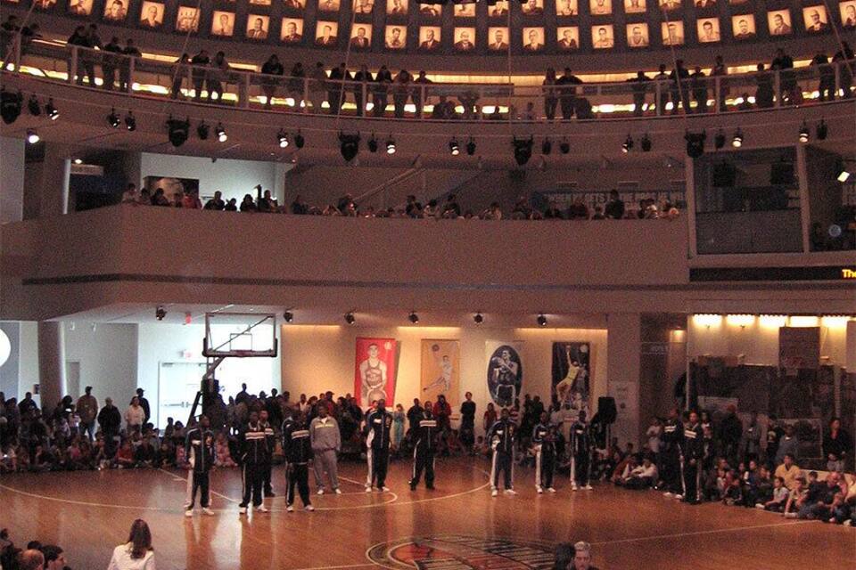 A basketball court with spectators, a scoreboard, and a wall of portraits.