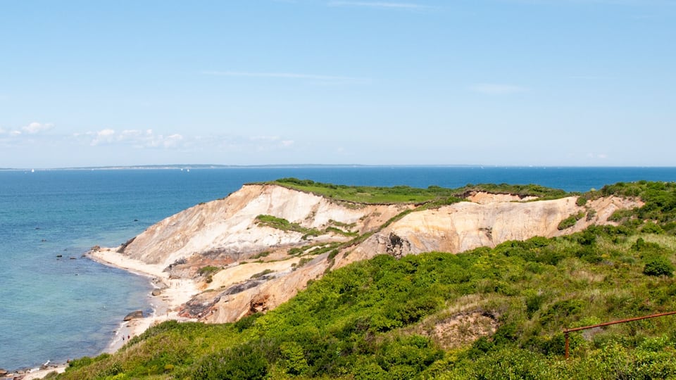 A coastal landscape with a lighthouse, cliffs, and a clear blue sea.