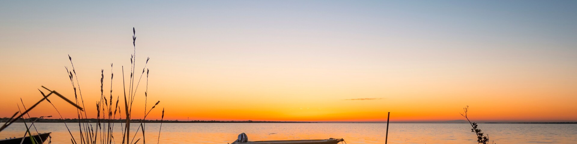 A sunset over a calm body of water with a small boat docked near the shore.