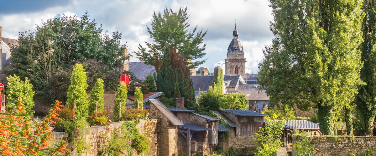 A canal with stone buildings, a church steeple, and lush greenery.