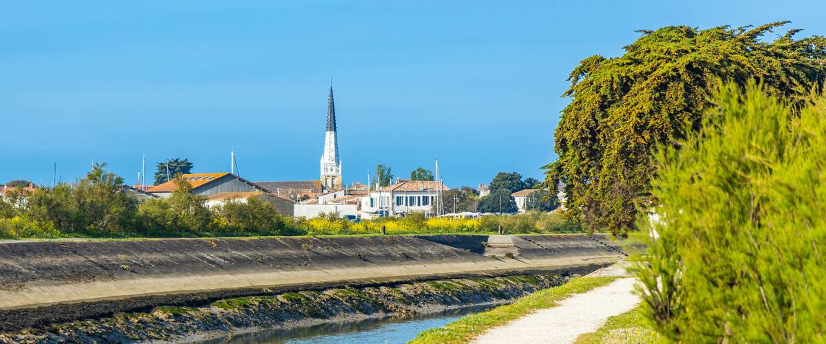 A coastal town with a prominent church spire, a canal, and lush greenery.