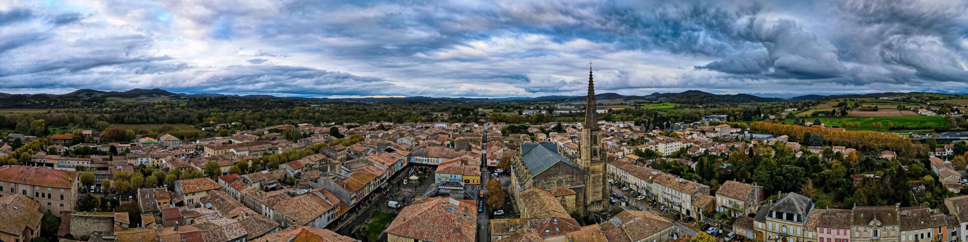 Uma cidade com edifícios históricos, uma torre de igreja imponente e colinas ondulantes ao fundo.