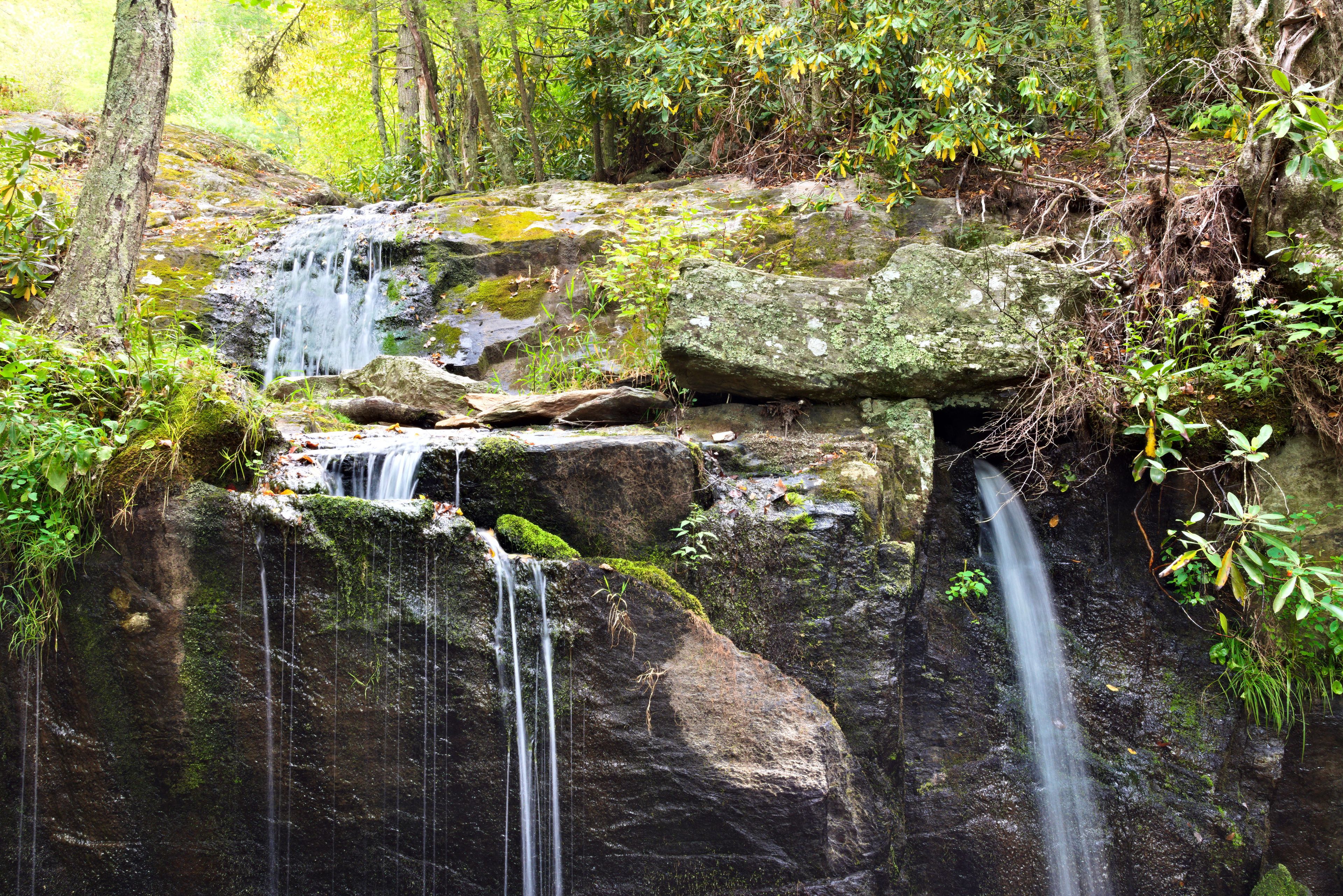 A multi-tiered waterfall cascading over moss-covered rocks in a forested area.