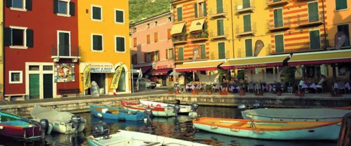 A waterfront with colorful buildings, boats docked, and a hill in the background.