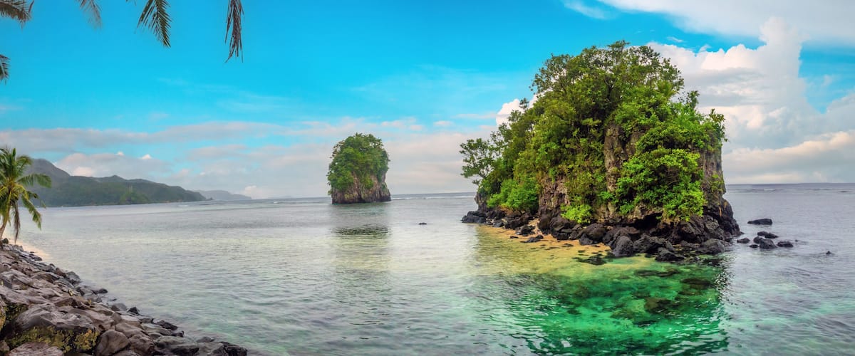 A tropical island with clear turquoise waters, rocky shorelines, and lush greenery.