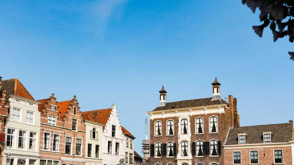 A row of historic European buildings with red and white facades, a tower, and a clear blue sky.