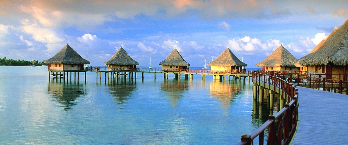 Overwater bungalows connected by a wooden walkway over calm blue water.