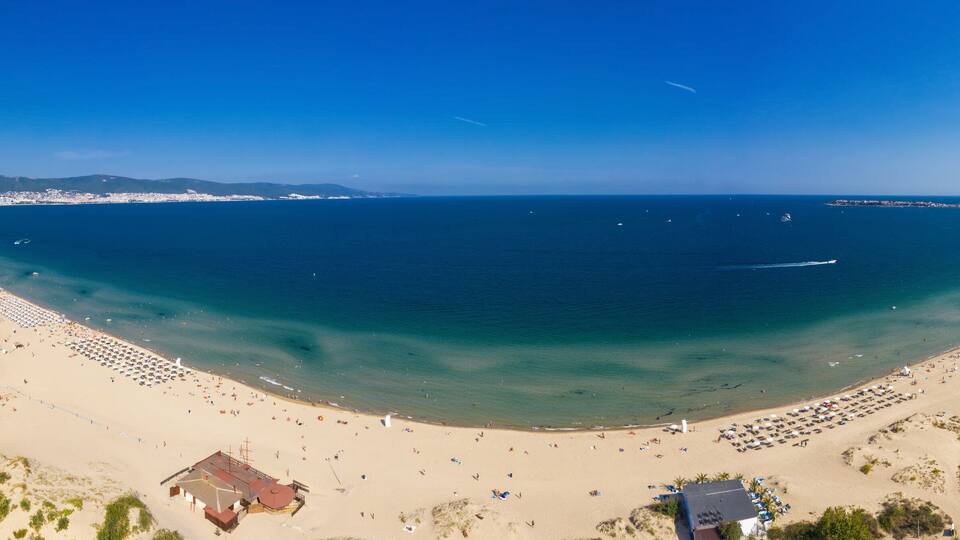 A coastal cityscape with a large beach, clear blue waters, and urban buildings.