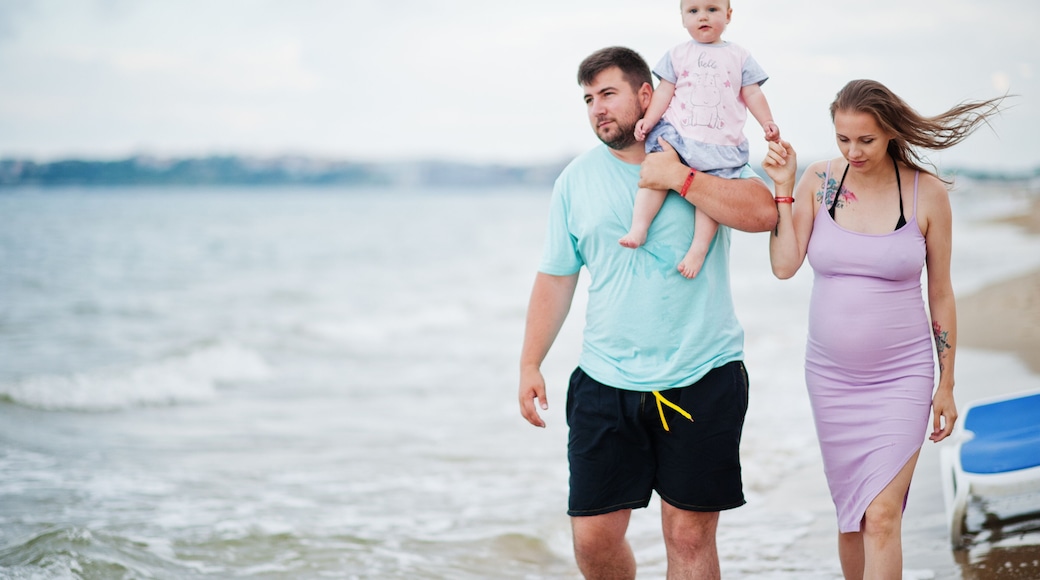 Summer vacations. Parents and people outdoor activity with children. Happy family holidays. Father, pregnant mother, baby daughter on sea sand beach.