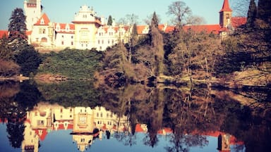 Un castillo con techo rojo y una torre, reflejado en aguas tranquilas.