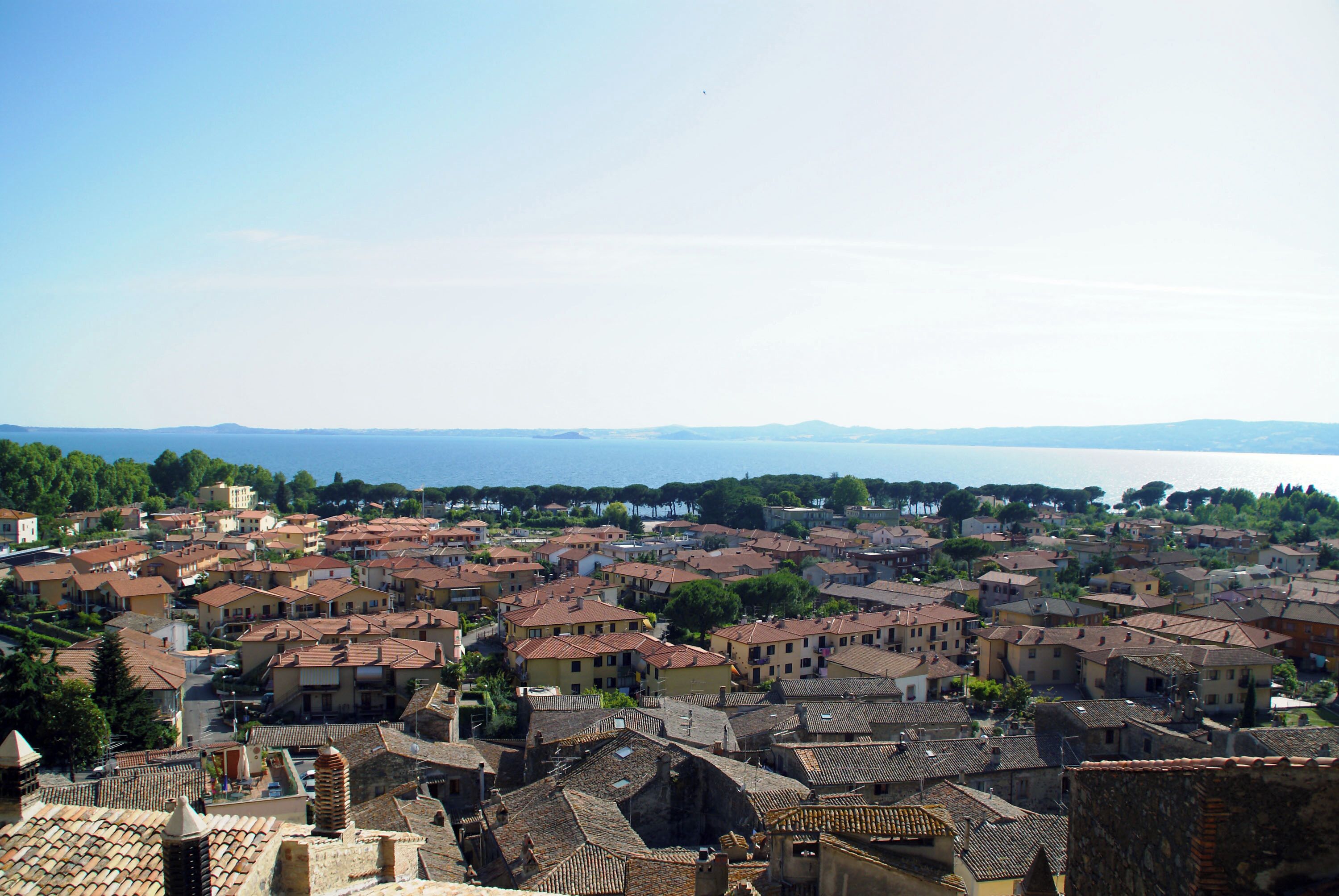 A coastal town with terracotta-roofed buildings, a clear sky, and a distant view of the sea.