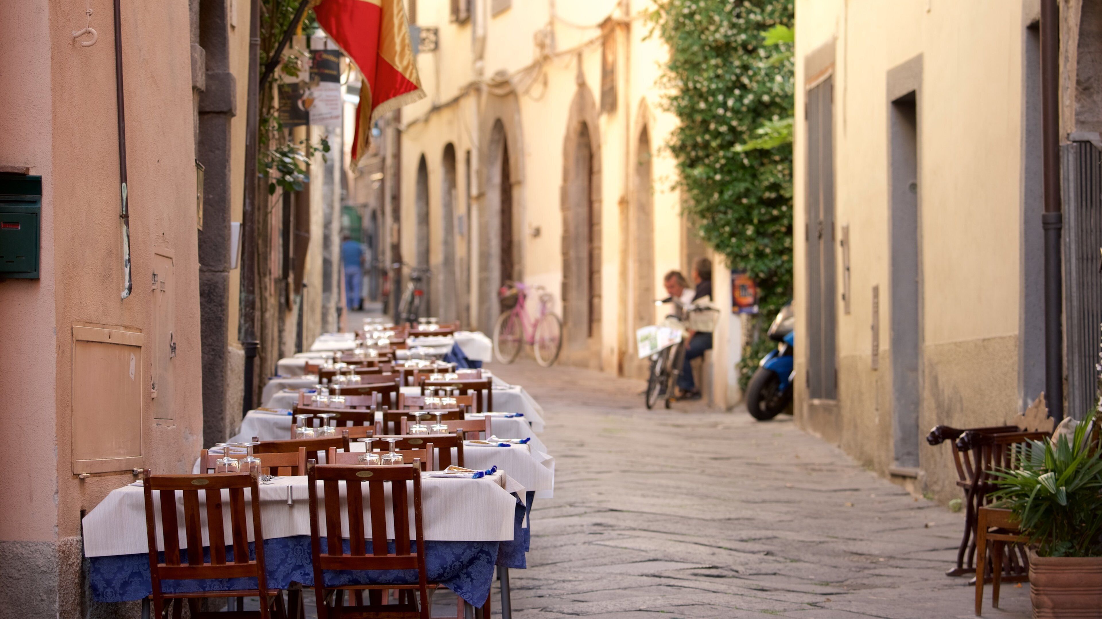 A row of tables set up on a cobblestone street with buildings on either side.