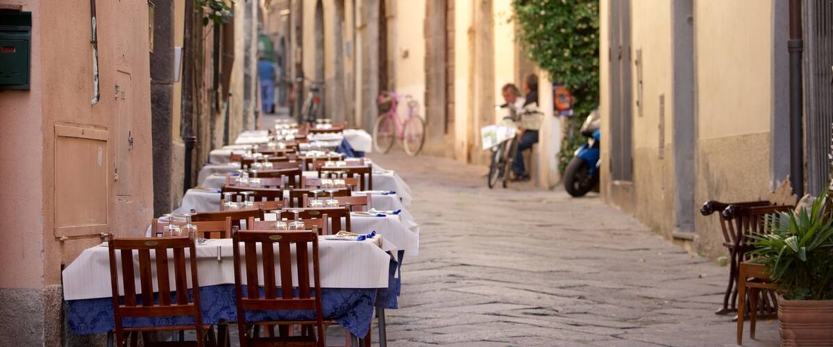 A row of tables set up on a cobblestone street with buildings on either side.