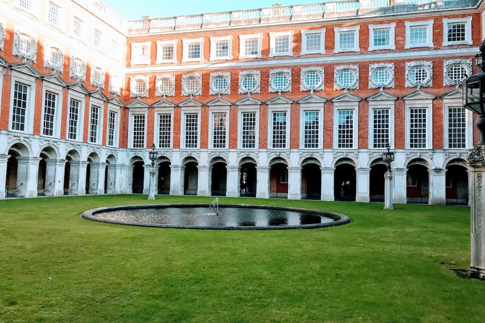 A large courtyard with a fountain, surrounded by red brick buildings with white windows and arches.