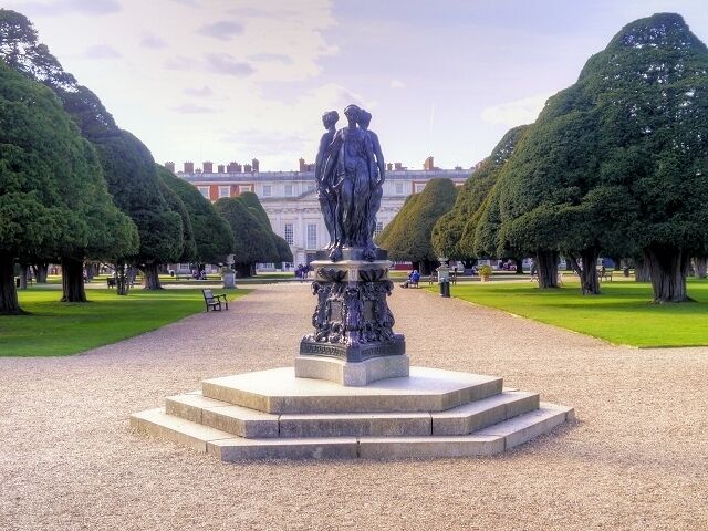 A statue in a park with neatly trimmed trees and a building in the background.