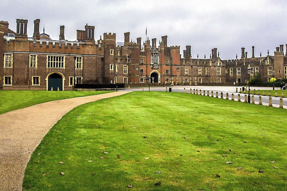 A large, historic brick building with a well-maintained lawn and a paved path leading to its entrance.