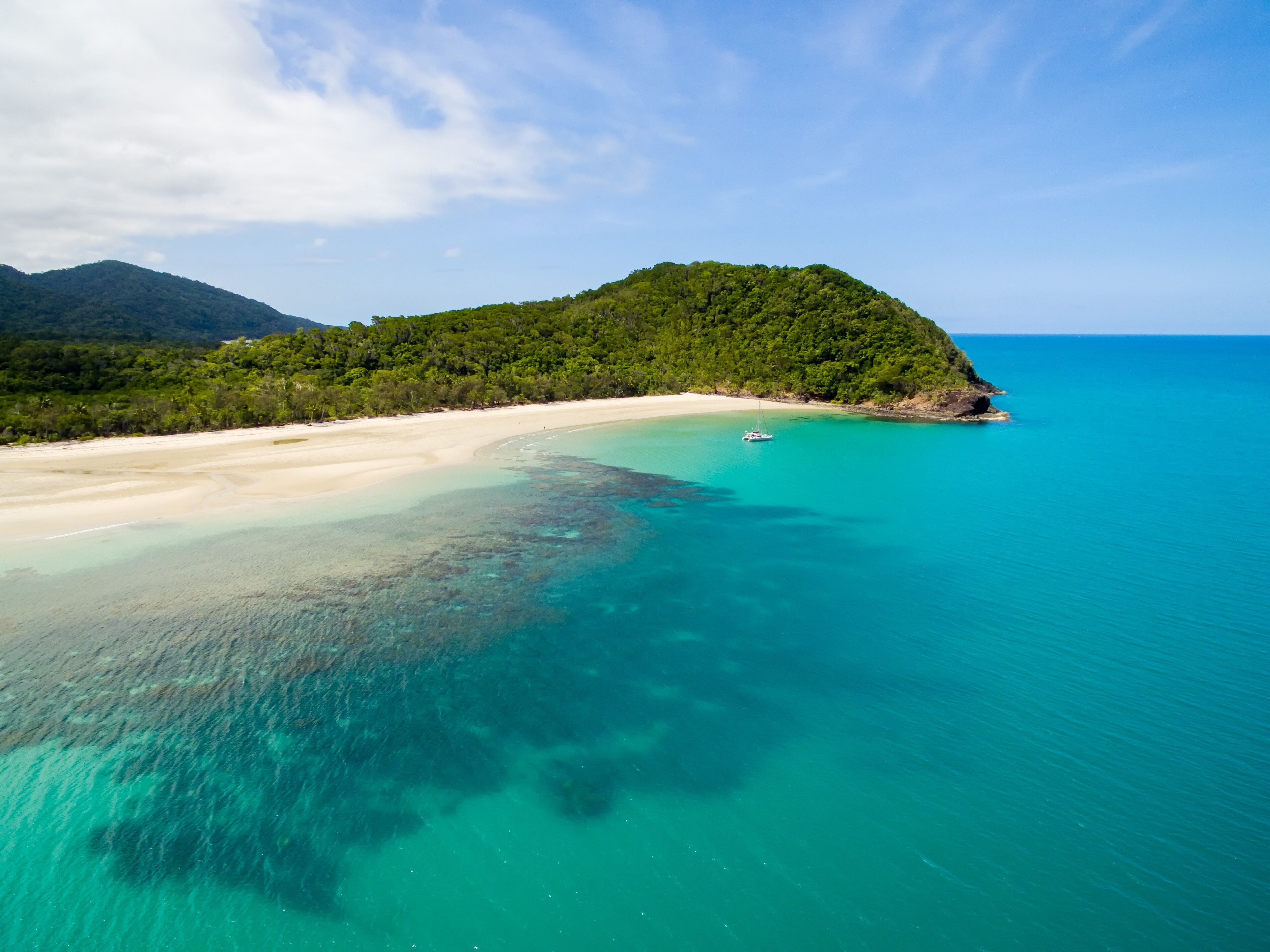 Uma praia tropical com águas turquesa cristalinas, areia dourada e uma colina verde exuberante ao fundo.