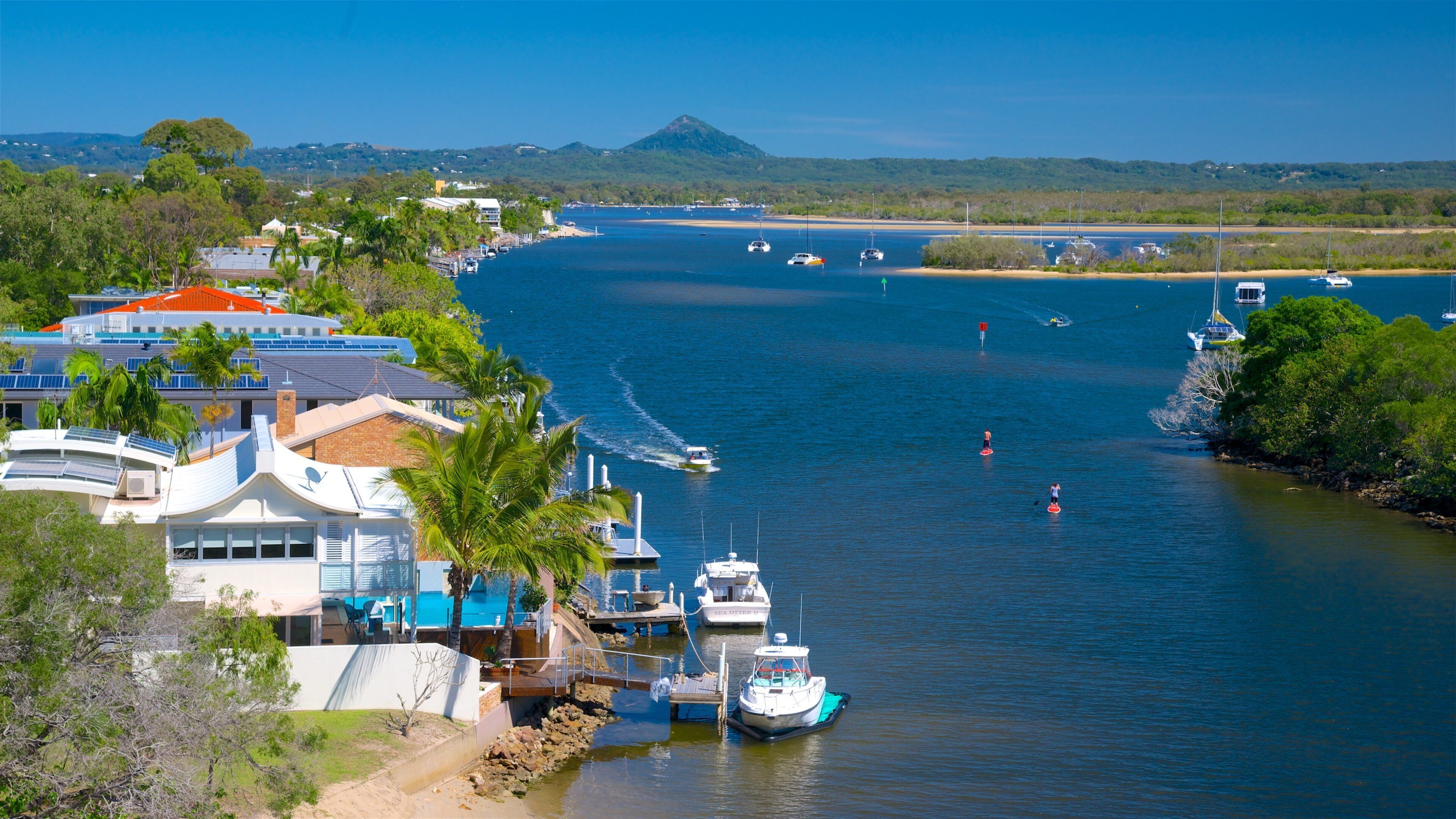 A coastal marina with boats, a beach, and a mountain in the background.