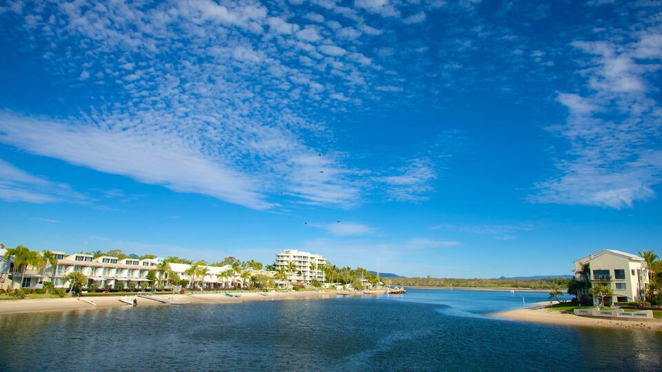 A coastal resort with beachfront villas, a sandy beach, and a calm sea under a partly cloudy sky.