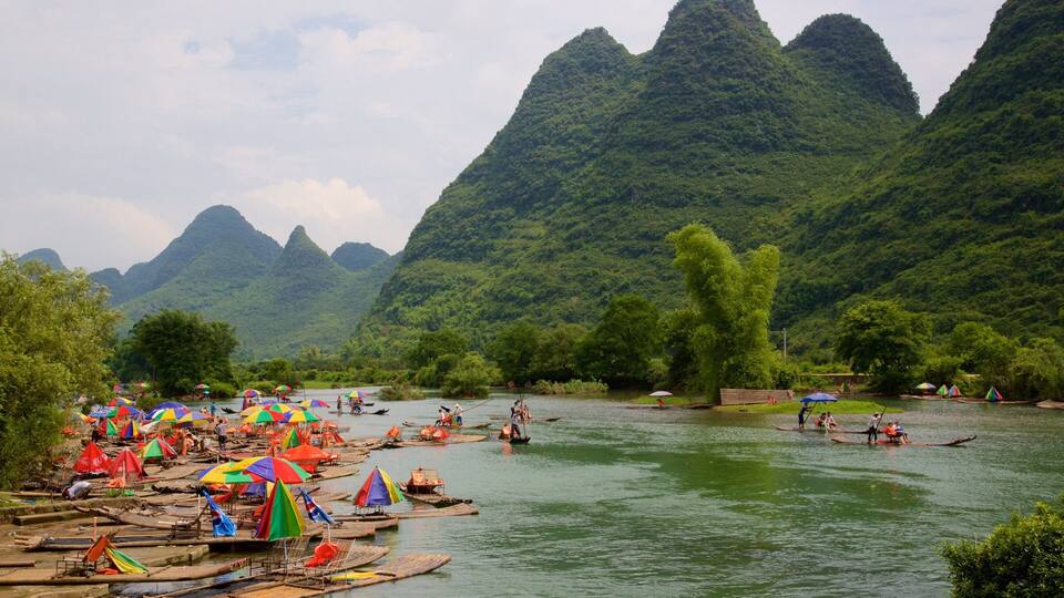A river with boats and colorful umbrellas, surrounded by lush green mountains.