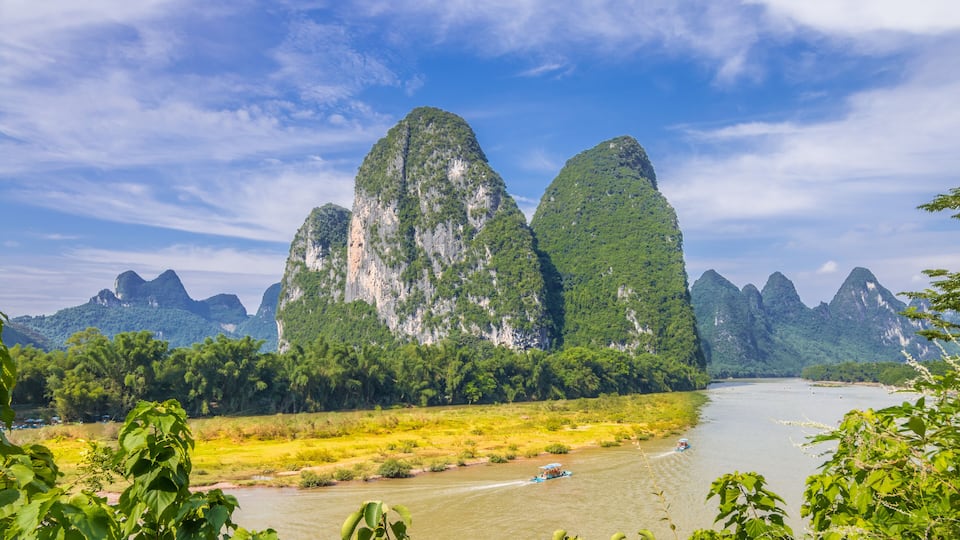 A river with a boat, surrounded by lush greenery and limestone karst mountains.